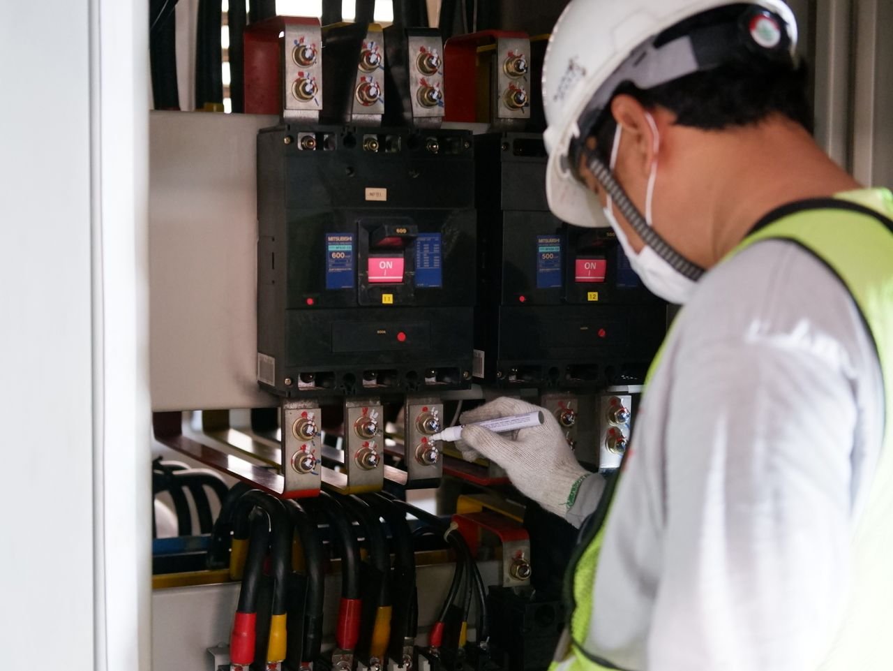 services-02 Technician wearing safety gear inspecting electrical panels in an industrial setting.