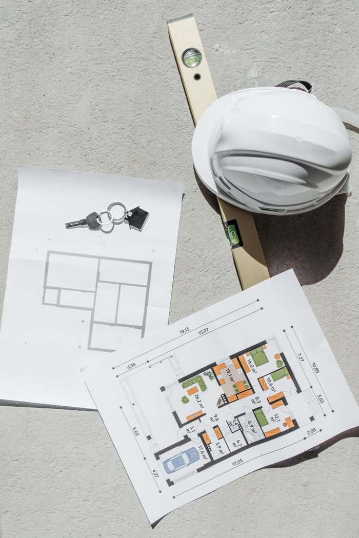Mengenal SLF Flat lay of construction plans, keys, hard hat, and level tool on concrete.